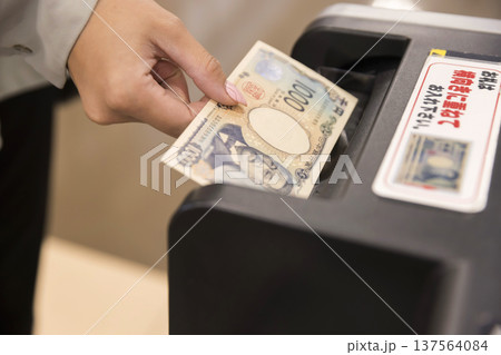 現金自動支払機にお金を投入する女性手元 現金自動支払機にお金を投入する女性手元 137564084