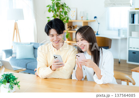リビングでスマホを見る若いカップル リビングでスマホを見る若いカップル 137564085