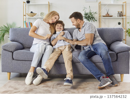 Happy family sitting on sofa, parents tickling laughing son, enjoying carefree time together at home 137564232