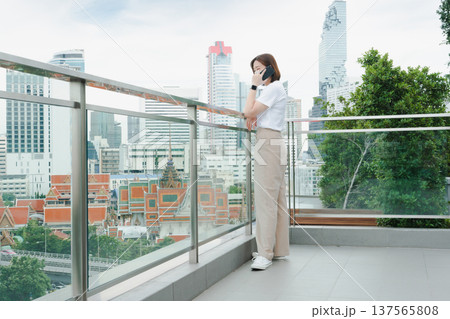solo asian woman during use phone and relax at rooftop with city background solo asian woman during use phone and relax at rooftop with city background 137565808