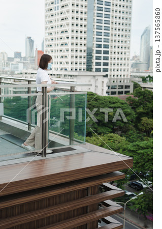 solo asian woman wear protective mask during outdoor break and relax at rooftop with city background 137565860