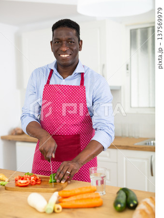 African american man in an apron cooks cuts vegetables for making soup in kitchen 137569979