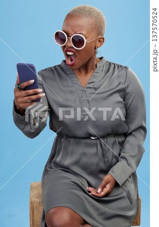 Phone, news and angry black woman shocked in studio frustrated by glitch, 404 or scam on blue background. Smartphone, fail and African female model annoyed with notification, phishing or spam email 137570524