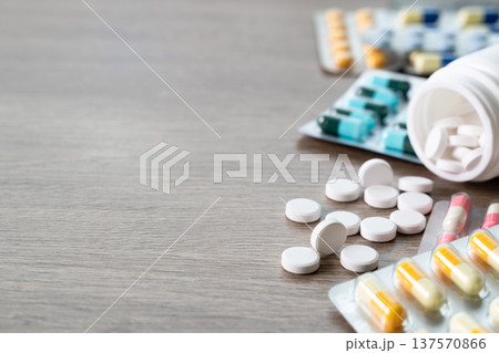 Concept of daily medication routine and chronic disease management. White tablets spilling from bottle with blister capsules on wooden table, symbol of prescription compliance and dosage control at 137570866