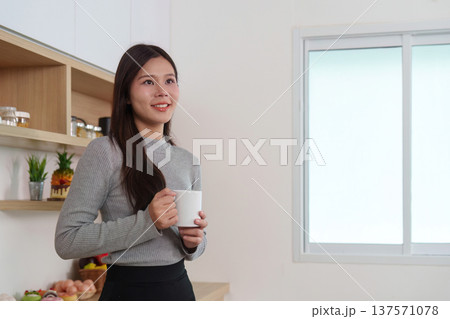 Morning routines. Young woman smiling with coffee in cozy kitchen. 137571078