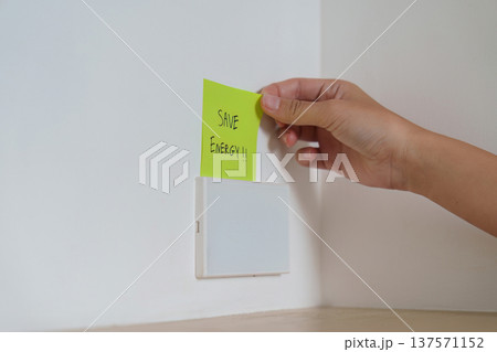 Energy Conservation. Woman placing reminder note to save energy on light switch. Energy Conservation. Woman placing reminder note to save energy on light switch. 137571152