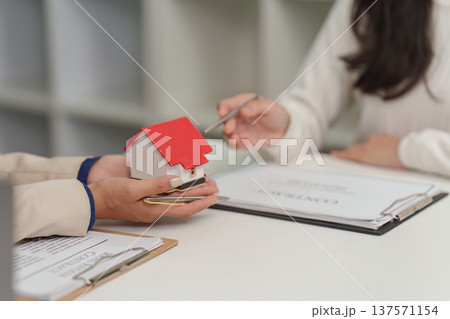 Real Estate Consultation. Client discussing home purchase with advisor using model house. Real Estate Consultation. Client discussing home purchase with advisor using model house. 137571154