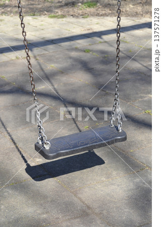 Empty black plastic swing hanging on metal chains in a playground Empty black plastic swing hanging on metal chains in a playground 137571278
