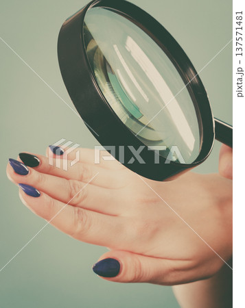 Woman looking at nails through magnifying glass 137571481