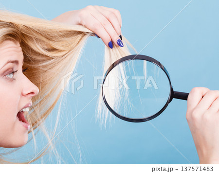 Woman looking at hair through magnifying glass 137571483