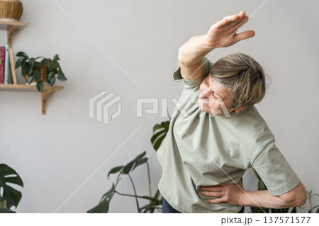Senior woman doing side bend stretching exercise, keeping fit and healthy at home for her wellbeing and vitality. Mindful happiness, an active, and healthy lifestyle 137571577