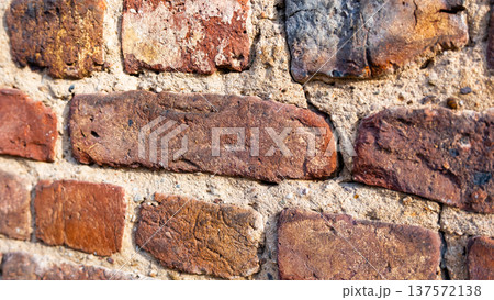 Textured brick wall with various shades of red and brown. The surface shows signs of wear and age, highlighting the rustic appearance of the bricks. Textured brick wall with various shades of red and brown. The surface shows signs of wear and age, highlighting the rustic appearance of the bricks. 137572138