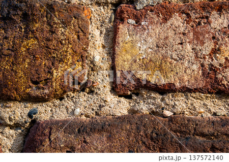 Textured brick wall with various shades of red and brown. The surface shows signs of wear and age, highlighting the rustic appearance of the bricks. Textured brick wall with various shades of red and brown. The surface shows signs of wear and age, highlighting the rustic appearance of the bricks. 137572140