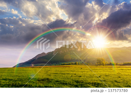 sunset over rock formation near green field. beautiful rural landscape in mountains. wonderful scenery lush grass in spring. clouds on the sky. alpine countryside outdoor adventure under rainbow sunset over rock formation near green field. beautiful rural landscape in mountains. wonderful scenery lush grass in spring. clouds on the sky. alpine countryside outdoor adventure under rainbow 137573780