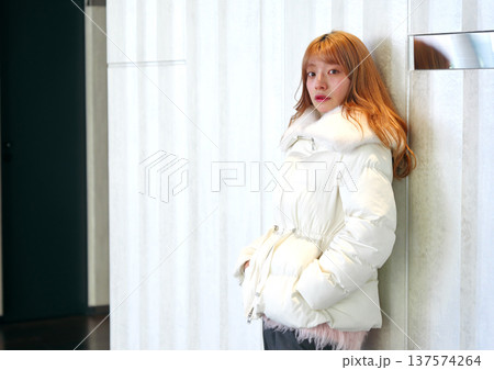 白い壁に寄り添う女性モデル。清潔感あふれる白いアウターと冬の洗練されたインドアポートレート。 137574264