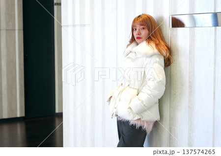 白い壁に寄り添う女性モデル。清潔感あふれる白いアウターと冬の洗練されたインドアポートレート。 137574265