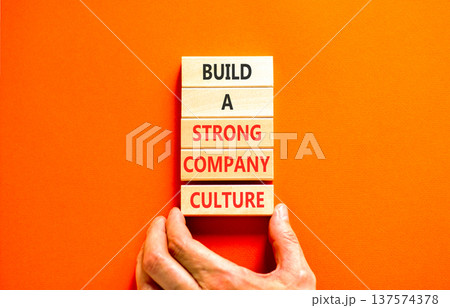 Strong company culture symbol. Concept words Build a strong company culture on beautiful wooden blocks. Beautiful orange paper background. Business strong company culture concept. Copy space. Strong company culture symbol. Concept words Build a strong company culture on beautiful wooden blocks. Beautiful orange paper background. Business strong company culture concept. Copy space. 137574378