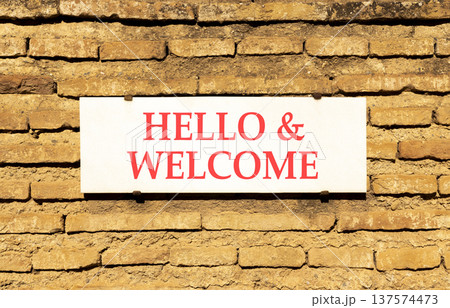 Hello and welcome symbol. Concept words Hello and welcome on beautiful big white sign plate. Beautiful old brown brick wall background. Business hello and welcome concept. Copy space. Hello and welcome symbol. Concept words Hello and welcome on beautiful big white sign plate. Beautiful old brown brick wall background. Business hello and welcome concept. Copy space. 137574473