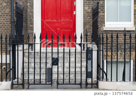 Traditional brick townhouse with a red door and iron fence representing classic British residential architecture in London. Traditional brick townhouse with a red door and iron fence representing classic British residential architecture in London. 137574658