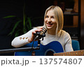 Young woman singing and playing acoustic guitar in recording studio 137574807
