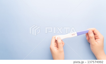 Pregnant woman holding a positive urine pregnancy test on blue background. Pregnancy test kit measure hCG levels in urine. Pregnant woman holding a positive urine pregnancy test on blue background. Pregnancy test kit measure hCG levels in urine. 137574992