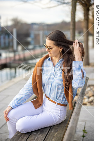 Elegant young woman in old money style sitting on bench near pier in Prague wearing sunglasses in early spring. Quiet luxury lifestyle and refined European elegance concept. Elegant young woman in old money style sitting on bench near pier in Prague wearing sunglasses in early spring. Quiet luxury lifestyle and refined European elegance concept. 137575098