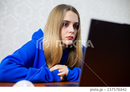 Shocked blonde girl stares wide eyed at laptop screen after reading shocking news online. She discovers unbelievable information that leaves her stunned and speechless at home Shocked blonde girl stares wide eyed at laptop screen after reading shocking news online. She discovers unbelievable information that leaves her stunned and speechless at home 137576842