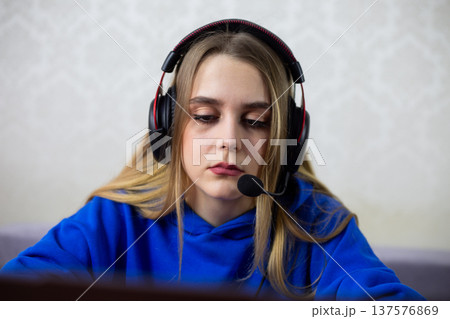 Exhausted young woman sits with poor posture at laptop, wearing headphones. She looks sad and unmotivated during long remote work or study session. Burnout and mental fatigue concept at home 137576869