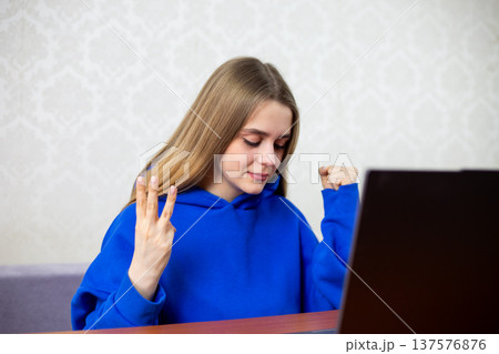 Blonde football fan celebrates third goal with three fingers raised toward laptop. She witnesses hat trick or decisive score during live match. Intense excitement at home Blonde football fan celebrates third goal with three fingers raised toward laptop. She witnesses hat trick or decisive score during live match. Intense excitement at home 137576876