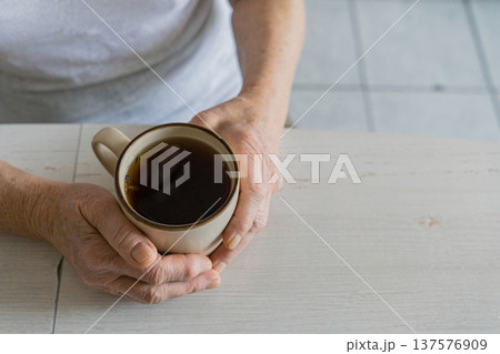 Senior person's wrinkled hands gently holding a hot mug of tea, finding comfort and warmth during a moment of relaxation Senior person's wrinkled hands gently holding a hot mug of tea, finding comfort and warmth during a moment of relaxation 137576909
