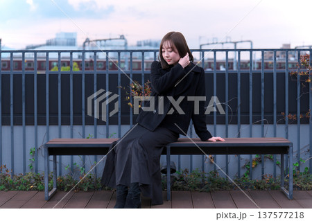 冬の空の下で佇む女性モデル。黒いコートが映える、叙情的でアンニュイな都会の屋外ポートレート。 冬の空の下で佇む女性モデル。黒いコートが映える、叙情的でアンニュイな都会の屋外ポートレート。 137577218