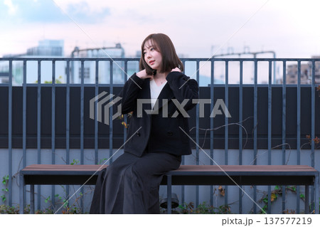 冬の空の下で佇む女性モデル。黒いコートが映える、叙情的でアンニュイな都会の屋外ポートレート。 冬の空の下で佇む女性モデル。黒いコートが映える、叙情的でアンニュイな都会の屋外ポートレート。 137577219
