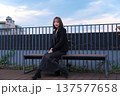 都会のテラスでベンチに座る黒コートの女性。洗練された冬の装いと穏やかな休日のポートレート。 137577658