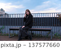 都会のテラスでベンチに座る黒コートの女性。洗練された冬の装いと穏やかな休日のポートレート。 137577660