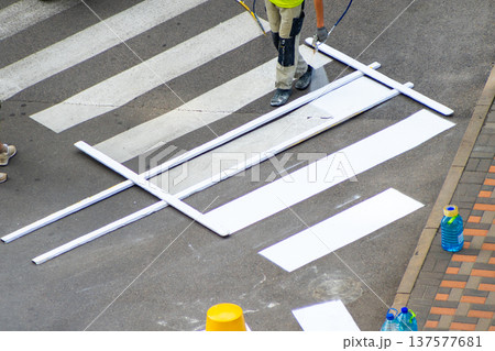 Road Worker Painting Pedestrian Crossing. Applying markings. Paint spray white color line. Highway crosswalk mark working man. 137577681