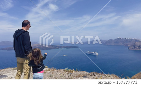 Journey to the caldera: panoramic view of the Aegean Sea from Santorini cliffs with father and daughter pointing at cruise ship Journey to the caldera: panoramic view of the Aegean Sea from Santorini cliffs with father and daughter pointing at cruise ship 137577773