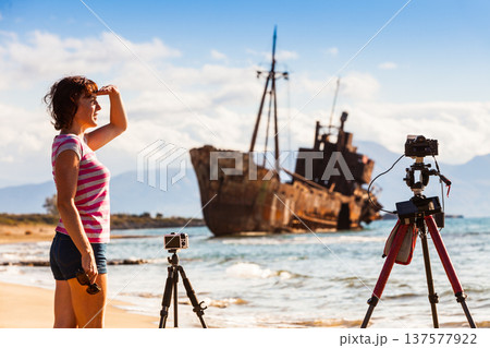 Woman with camera on tripod and shipwreck Woman with camera on tripod and shipwreck 137577922
