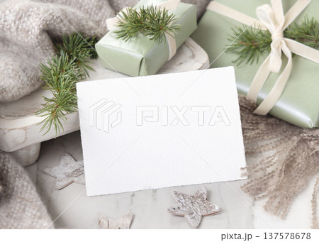 Horizontal Christmas card mockup on wrapped light green gift box with fir branch near beige blanket 137578678