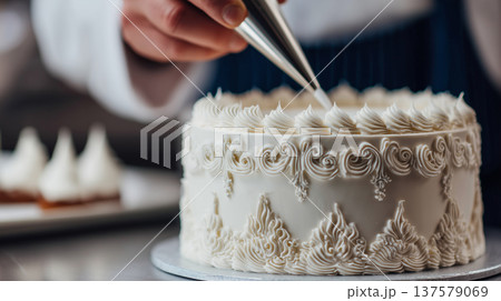 Pastry chef decorating white cream cake with piping bag elegant dessert confectionery preparation closeup 137579069