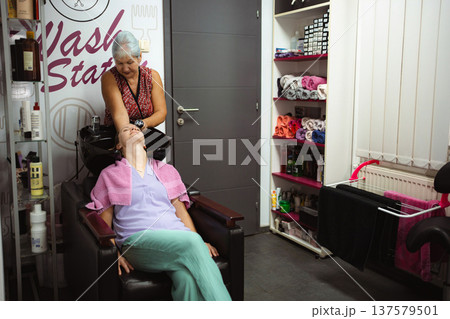 Hairdresser washing client's hair at salon sink for treatment Hairdresser washing client's hair at salon sink for treatment 137579501