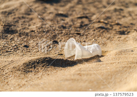 Discarded plastic cup lying on sandy beach symbolizing pollution and environmental problem 137579523