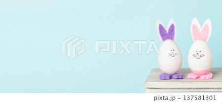 Decorative Easter eggs with bunny ears on wooden surface, pastel background Decorative Easter eggs with bunny ears on wooden surface, pastel background 137581301