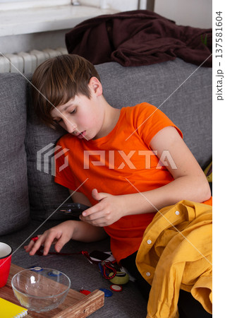 Boy in orange shirt rests on sofa while playing with tools on a lazy afternoon Boy in orange shirt rests on sofa while playing with tools on a lazy afternoon 137581604