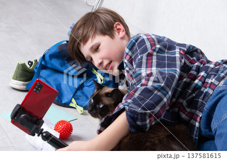 Young boy enjoys playful moment with cat while recording on smartphone in cozy indoor setting Young boy enjoys playful moment with cat while recording on smartphone in cozy indoor setting 137581615