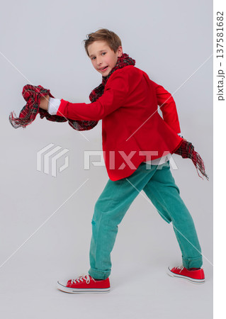 Funny boy in a red jacket, green jeans and sneakers in full growth on a gray background. He takes a big step with his leg up. The concept is only forward. Funny boy in a red jacket, green jeans and sneakers in full growth on a gray background. He takes a big step with his leg up. The concept is only forward. 137581682