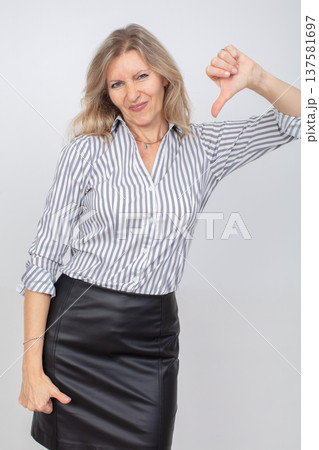 Woman expressing disapproval in a striped shirt and leather skirt against a plain background 137581697