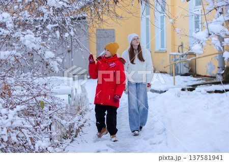 A boy and a girl in winter clothes are walking in front of a house. A boy and a girl in winter clothes are walking in front of a house. 137581941