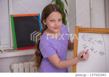 Young girl joyfully solving math problems on a chalkboard in a bright classroom setting 137581943