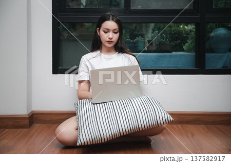 A young woman with laptop and pillow sitting drowsy on the living room floor. A young woman with laptop and pillow sitting drowsy on the living room floor. 137582917