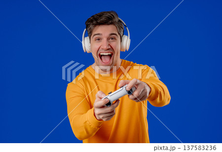Excited Gamer Man Playing Online Video Game On Console With Gamepad On Blue 137583236